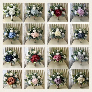 K&ouml;nnte beinhalten: Eine Sammlung von sechzehn k&uuml;nstlichen Hochzeitsstr&auml;u&szlig;en mit verschiedenfarbigen Hortensienbl&uuml;ten, wei&szlig;en Rosen und gr&uuml;nem Eukalyptuslaub. Jeder Strau&szlig; ist mit einem Stielband gebunden und zeigt eine vielf&auml;ltige Farbpalette.
