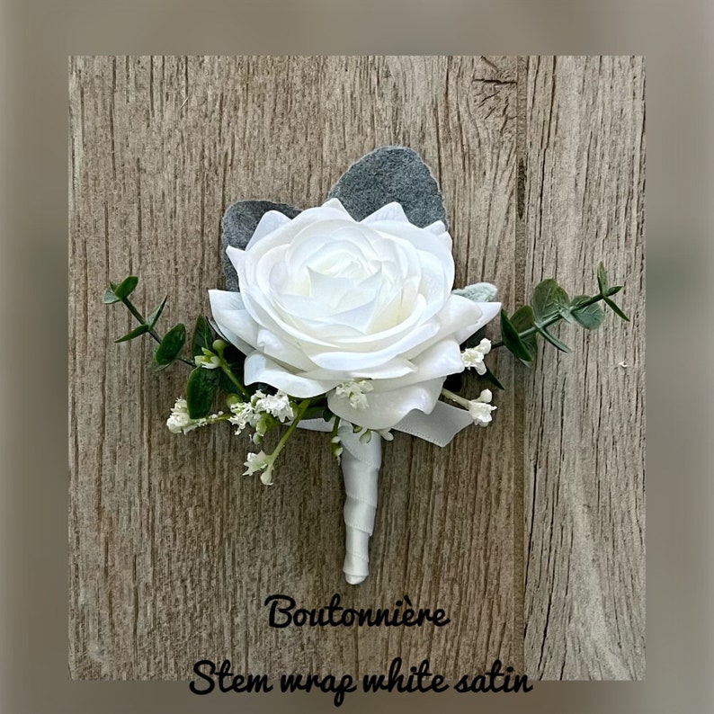 May include: White rose boutonniere with eucalyptus greenery and white satin stem wrap. The text "Boutonni&egrave;re" and "Stem wrap white satin" is printed below the flower.