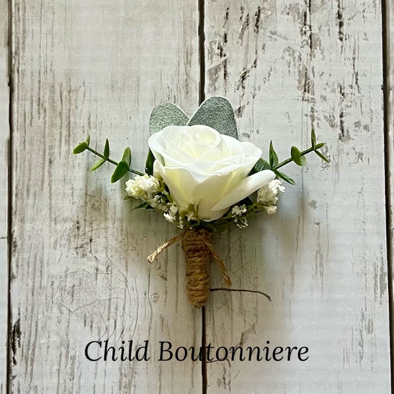May include: A boutonniere featuring a single white rose, small white filler flowers, and green eucalyptus leaves. The stem is wrapped in brown twine. The text Child Boutonniere is printed at the bottom of the image in a black serif font.