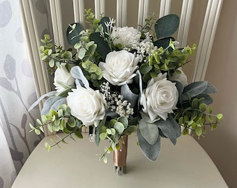May include: A white bridal bouquet with white roses, greenery, and sprigs of baby's breath.