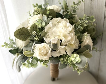 May include: A white bridal bouquet with white roses, hydrangeas, and greenery.