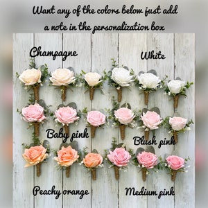 May include: A collection of eighteen floral boutonnieres arranged in three rows, featuring roses in champagne, white, baby pink, blush pink, peachy orange, and medium pink. Each boutonniere includes green eucalyptus leaves and twine-wrapped stems.