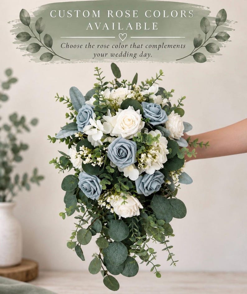 Op de afbeelding: Een watervalboeket met stoffige blauwe en witte rozen, afgewisseld met kleine witte vulbloemen en diverse groene eucalyptusbladeren. De tekst bovenaan luidt: CUSTOM ROSE COLORS AVAILABLE. Choose the rose color that complements your wedding day.