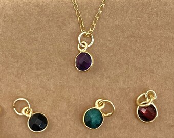 May include: A set of six gold-tone pendants with different colored gemstones. The pendants feature a variety of colors, including purple, green, red, and clear.