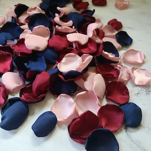 May include: A pile of silk rose petals in navy blue, burgundy, and blush pink colors. The petals are scattered on a white surface.