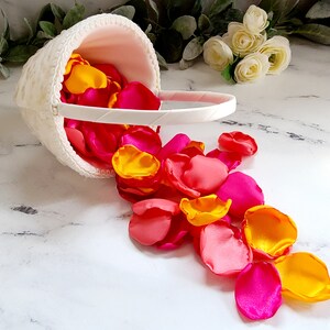 Puede incluir: Una cesta blanca llena de p&eacute;talos de flores rosas y amarillos. Los p&eacute;talos se derraman de la cesta sobre una superficie blanca.