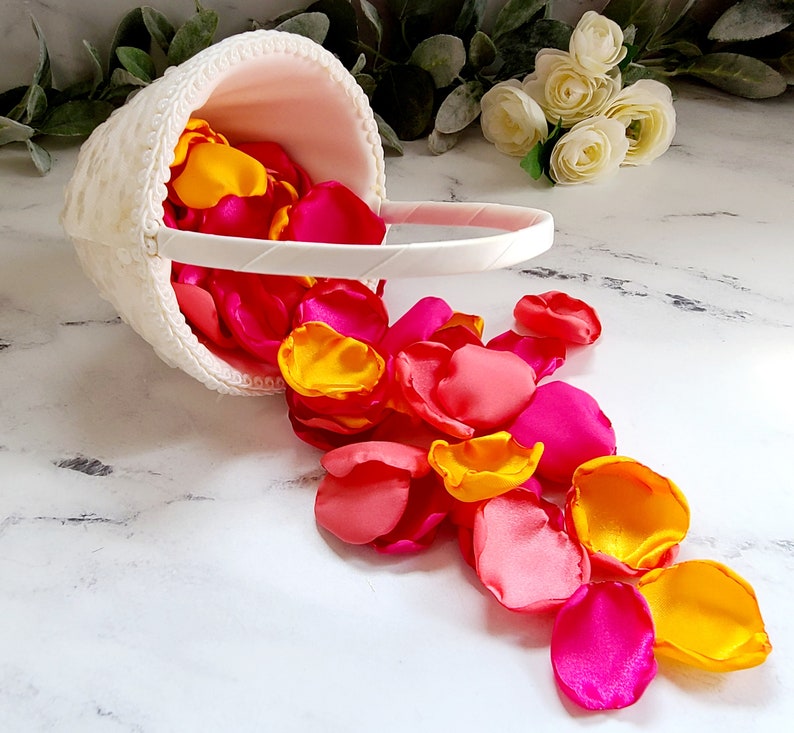 Puede incluir: Una cesta blanca llena de p&eacute;talos de flores rosas y amarillos. Los p&eacute;talos se derraman de la cesta sobre una superficie blanca.