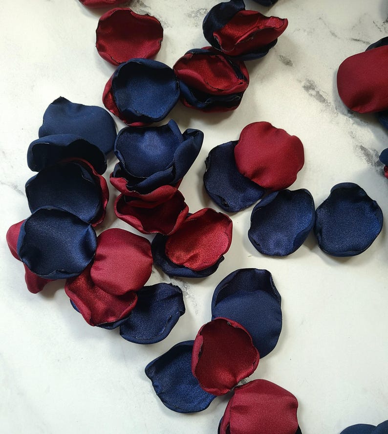 May include: A pile of navy blue and burgundy satin rose petals. The petals are arranged in a random pattern and are perfect for wedding decorations or other special events.