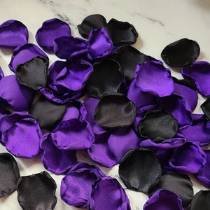 May include: A pile of purple and black satin rose petals. The petals are arranged in a random pattern and are perfect for decorating a wedding or other special event.