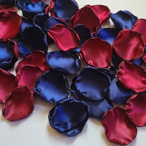 May include: A pile of burgundy and navy blue silk rose petals. The petals are scattered on a white surface.