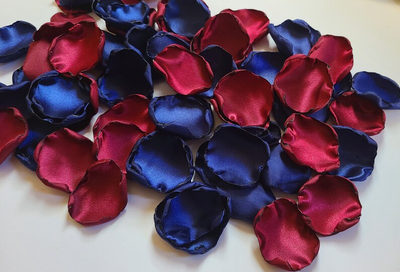 May include: A pile of burgundy and navy blue silk rose petals. The petals are scattered on a white surface.