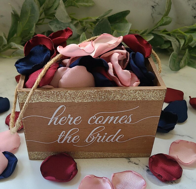 May include: A wooden box with a gold glitter trim and the text "here comes the bride" in white lettering. The box is filled with pink, burgundy, and navy blue fabric flower petals.