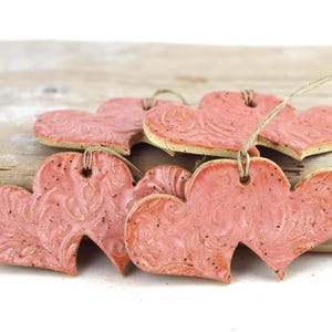 May include: A set of six pink ceramic heart ornaments with a textured design. The hearts are strung together with twine.