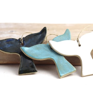 Peut inclure: Trois ornements en céramique en forme de queue de baleine, en bleu, blanc et noir. Chaque queue est munie d'une boucle en ficelle pour la suspension.