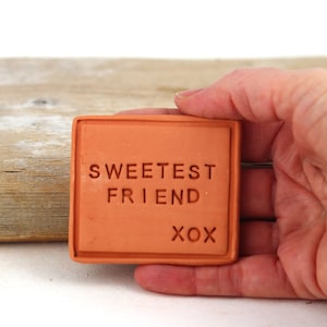 May include: A terracotta tile with the words "Sweetest Friend" and "xox" engraved on it.