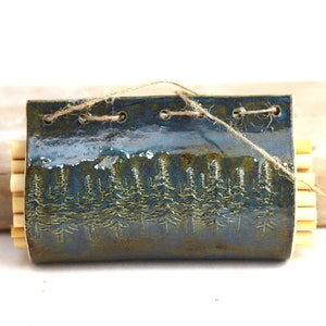 May include: A blue and green ceramic wall planter with a tree design and a string tied around it. The planter is filled with wooden dowels.