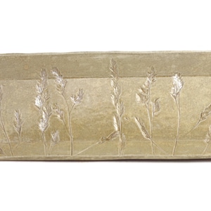 May include: A rectangular ceramic serving tray in a muted beige colour. The tray features an embossed design of tall grass or wheat stalks. The edges are slightly raised, and the overall shape is rectangular.