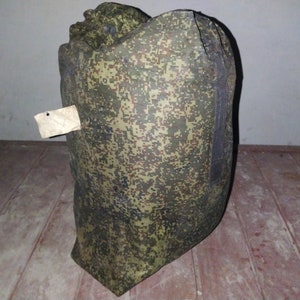 May include: A large, green and brown camouflage duffel bag with a black zipper and a small white tag attached.