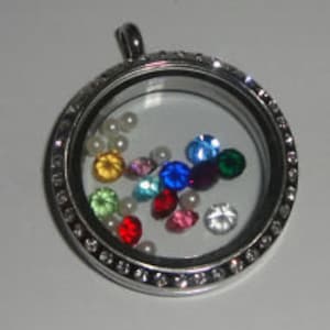 May include: Silver locket pendant with a clear glass window and a silver bezel. The locket is filled with colorful gemstones and white pearls.