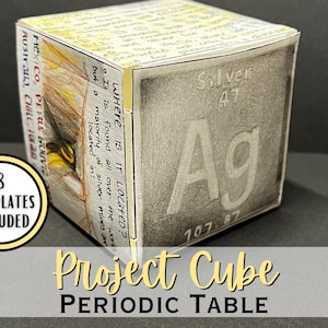 Puede incluir: Un proyecto educativo en forma de cubo etiquetado como "Project Cube Periodic Table". Un lado presenta el elemento Plata (Ag), número atómico 47 y masa atómica 107,87. El cubo incluye 8 plantillas. Los lados tienen texto e ilustraciones manuscritos.