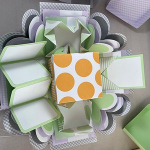 Pode incluir: Uma caixa de explos&atilde;o verde, cinza e roxa com uma caixa amarela e branca de bolinhas dentro. A caixa tem v&aacute;rias camadas e &eacute; perfeita para uma ocasi&atilde;o especial.