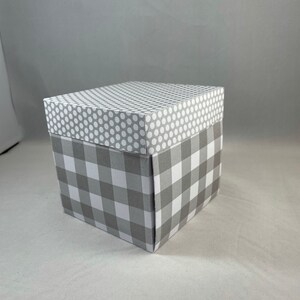 Pode incluir: Uma caixa de presente cinza e branca com um padr&atilde;o xadrez na parte inferior e um padr&atilde;o de bolinhas brancas na parte superior.