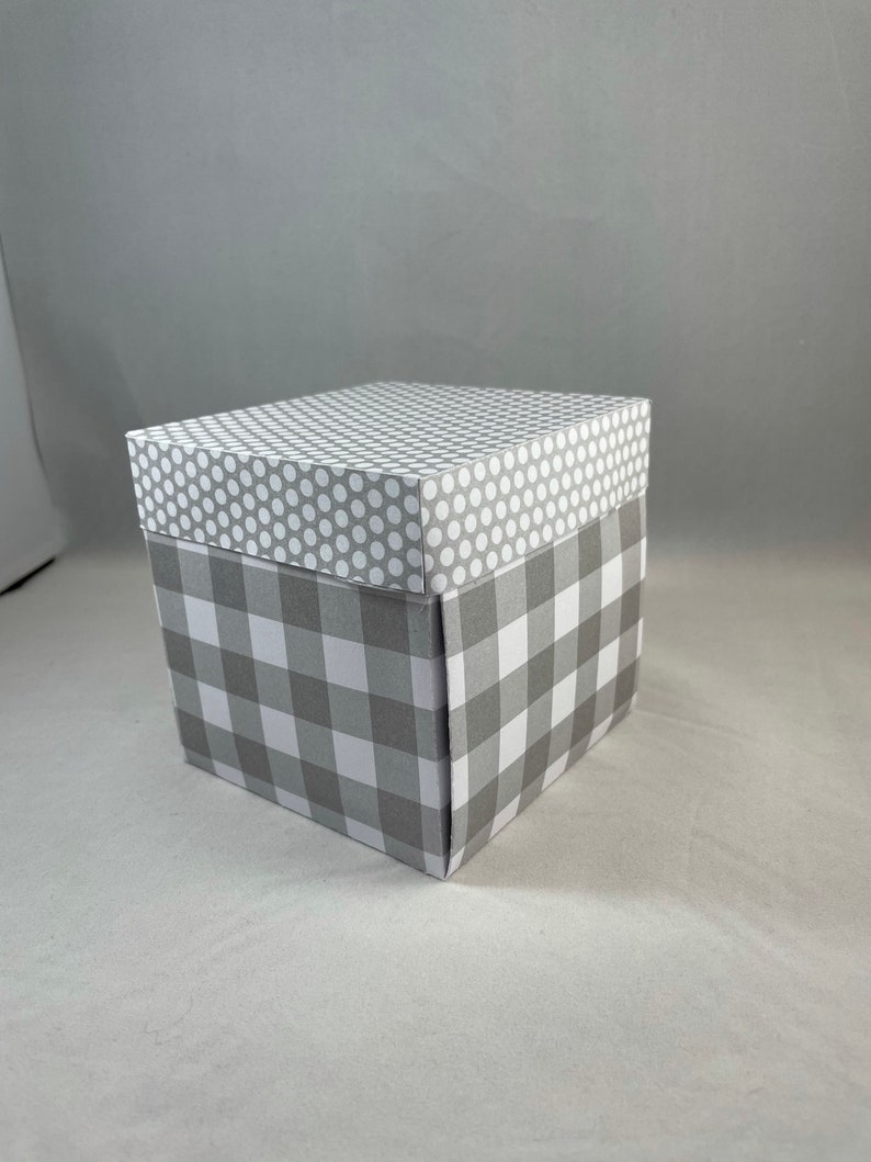 Pode incluir: Uma caixa de presente cinza e branca com um padr&atilde;o xadrez na parte inferior e um padr&atilde;o de bolinhas brancas na parte superior.