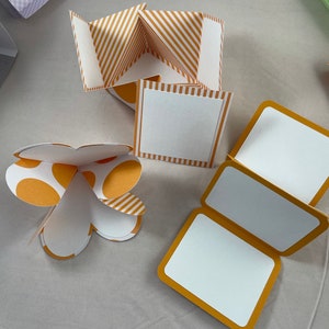 Pode incluir: Tr&ecirc;s caixas de artesanato de papel diferentes com padr&otilde;es de listras e bolinhas amarelas e brancas. As caixas est&atilde;o dobradas e prontas para serem montadas.