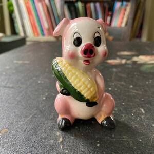 Pequeño y divertido cerdo caricaturesco sosteniendo una mazorca de maíz