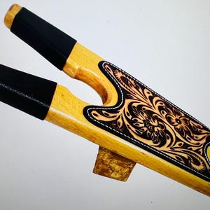 May include: A wooden boot jack with black leather straps and a tooled leather insert with a floral design.