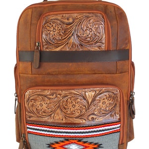 May include: Brown leather backpack with floral tooled detailing and a Southwestern-style woven panel. Features include multiple zipped compartments, a top handle, and adjustable straps. The bag has a rustic, vintage aesthetic.