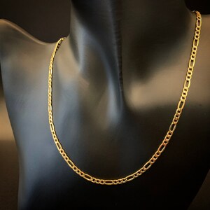 May include: A gold chain necklace with a figaro link pattern. The chain is on a black mannequin.