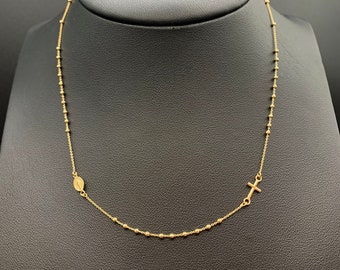 May include: A gold chain necklace with a small cross and a round pendant. The chain is made of small beads.