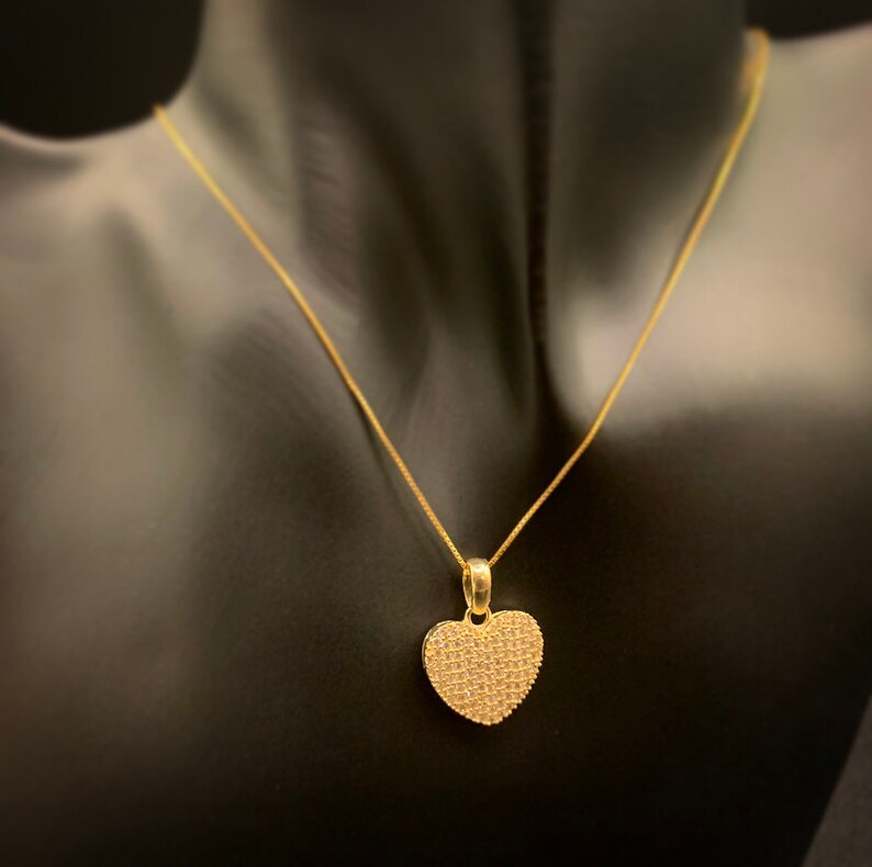 May include: A gold chain necklace with a heart-shaped pendant. The pendant is covered in small, sparkling stones.