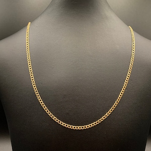May include: A gold-colored curb chain necklace displayed on a black mannequin. The chain is made of interlocking links, creating a continuous loop. The necklace is a simple, elegant piece of jewelry.