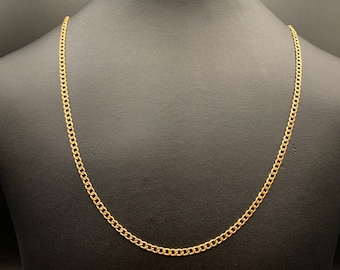 May include: A gold-colored curb chain necklace displayed on a black mannequin. The chain is made of interlocking links, creating a continuous loop. The necklace is a simple, elegant piece of jewelry.