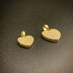 May include: Two gold heart-shaped pendants with a pave setting of small clear stones.