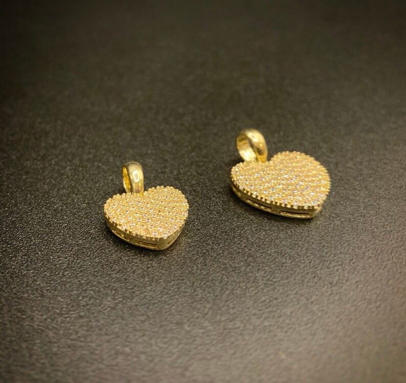 May include: Two gold heart-shaped pendants with a pave setting of small clear stones.