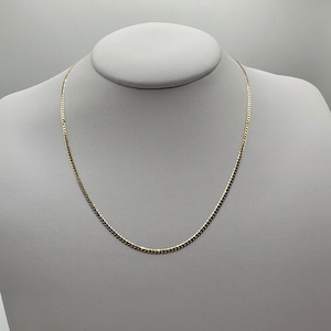 May include: A gold chain necklace with a curb link style. The chain is on a white mannequin.