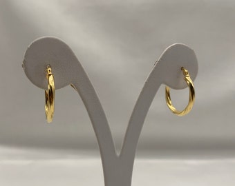 Pode incluir: Um par de brincos de argola de ouro com um design trançado. Os brincos são exibidos em um suporte branco.