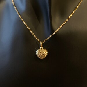 May include: A gold chain necklace with a heart-shaped pendant. The pendant is textured and has a diamond-like pattern.