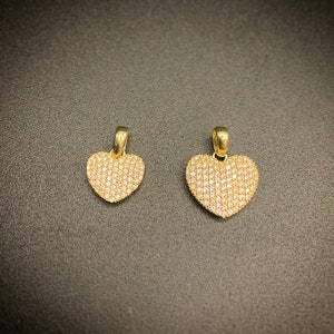 May include: Two gold heart-shaped pendants with a pave setting of clear stones.