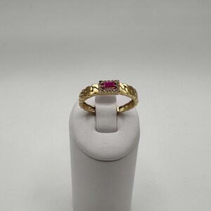 May include: A gold ring with a red ruby stone set in a square frame of smaller diamonds. The band of the ring is a chain link design.