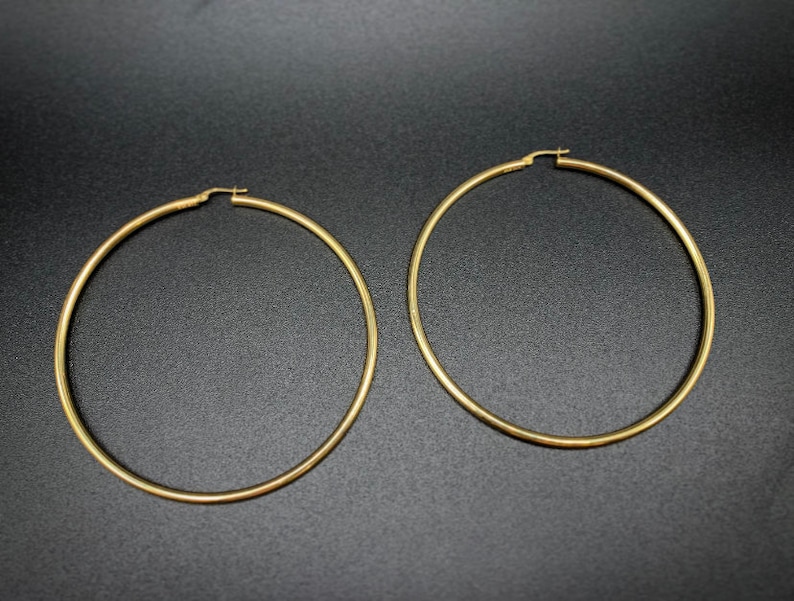 Pode incluir: Um par de brincos de argola de ouro. Os brincos s&atilde;o grandes e de forma circular.