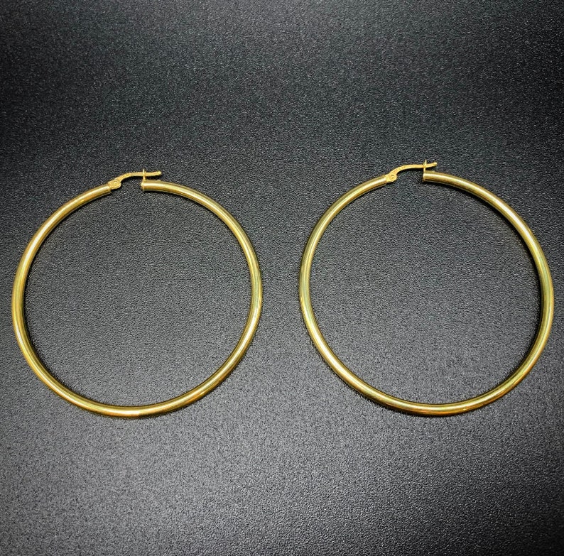 Pode incluir: Um par de brincos de argola de ouro. Os brincos s&atilde;o grandes e de forma circular.