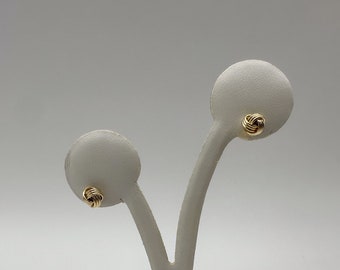 May include: A pair of gold knot-shaped stud earrings displayed on a white stand.