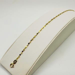 May include: A gold chain bracelet with a delicate, flat link design. The bracelet is on a white display stand.