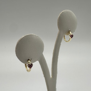 May include: A pair of gold hoop earrings with a small heart-shaped charm set with pink stones.