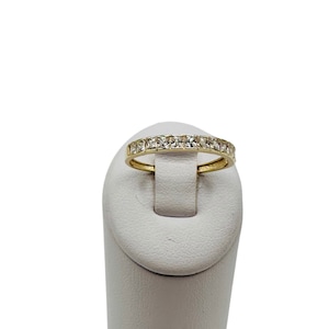 May include: A gold band ring with a row of square-shaped clear stones.