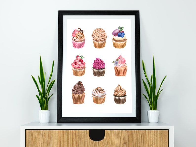 May include: A framed print featuring watercolor illustrations of nine cupcakes with various toppings. The cupcakes have pink, brown, and white frosting, and are decorated with berries, chocolate, and other decorative elements. The print is displayed on a white surface.